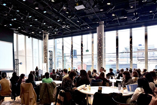 The audience watching as Dr. Shaheen Darani welcomes them to DWED 2025 in a large auditorium with floor-to-ceiling windows.