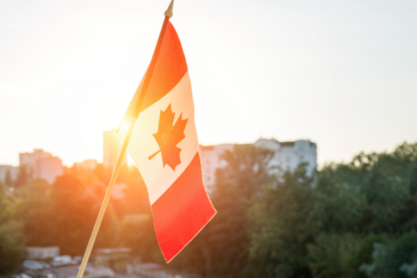A Canadian flag hangs outside, catching the light of the sun that is rising in the background..