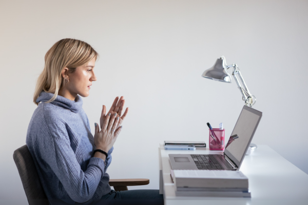 A woman sitting at a desk, speaking animatedly into a laptop.