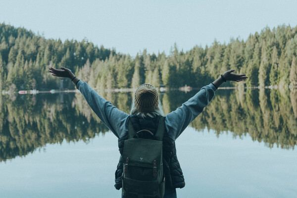 A woman raises her arms joyfully as she stands in front of a beautiful landscape.
