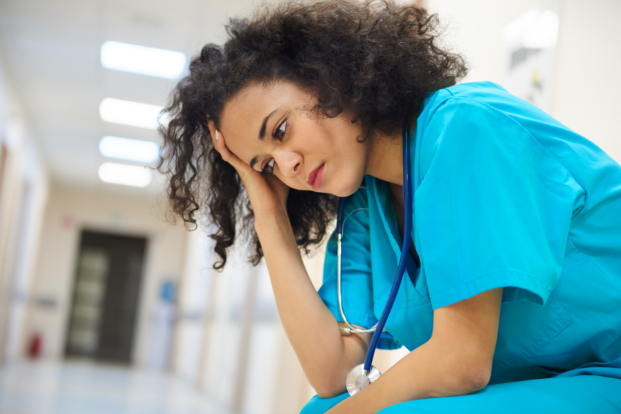A stressed health care work kneels in a hallway, her hand on her head