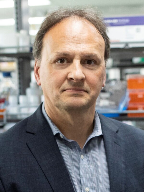 Dr. Etienne Sibille standing in front of a shelf filled with laboratory equipment while wearing a suit