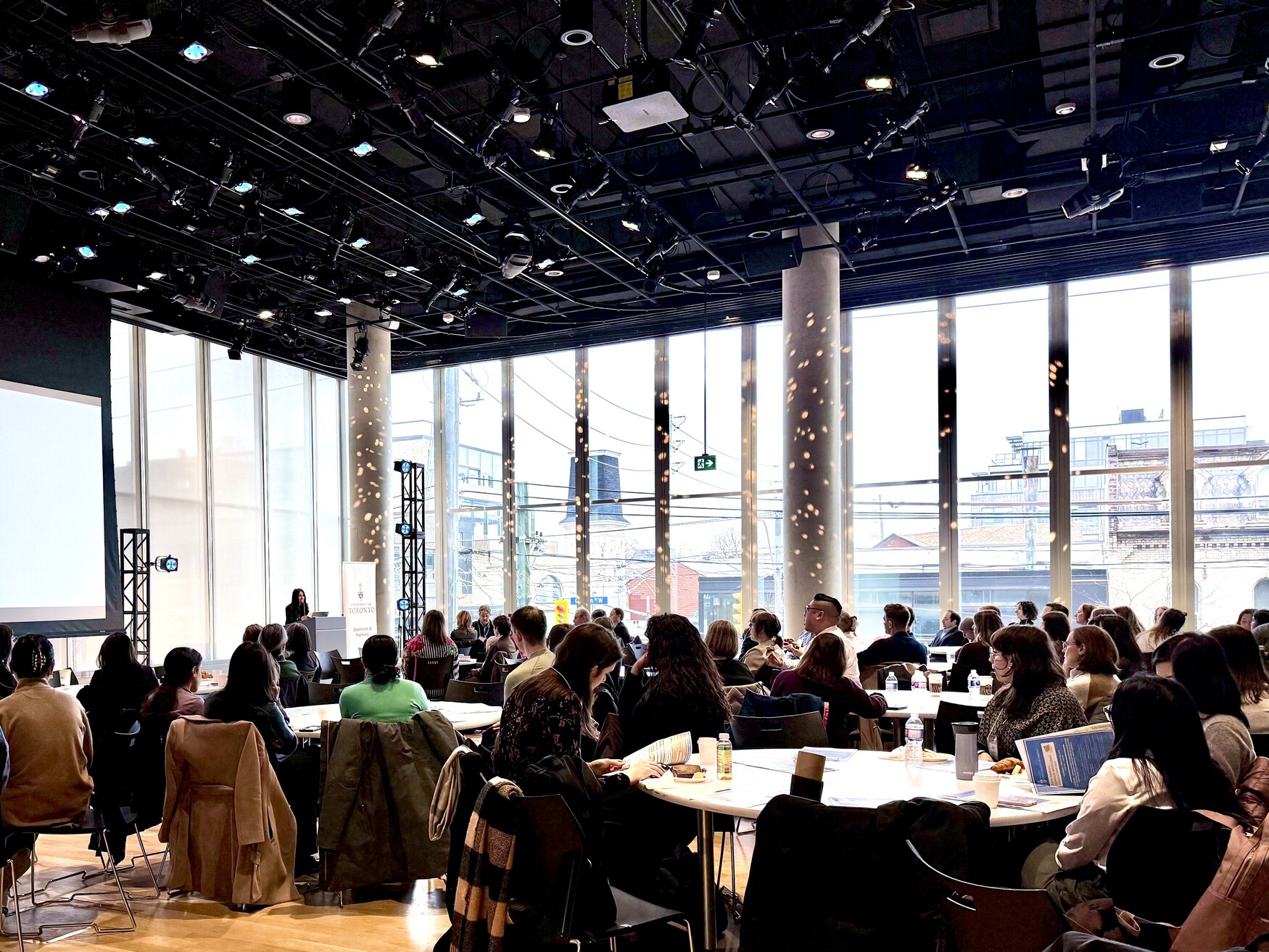 The audience watching as Dr. Shaheen Darani welcomes them to DWED 2025 in a large auditorium with floor-to-ceiling windows.