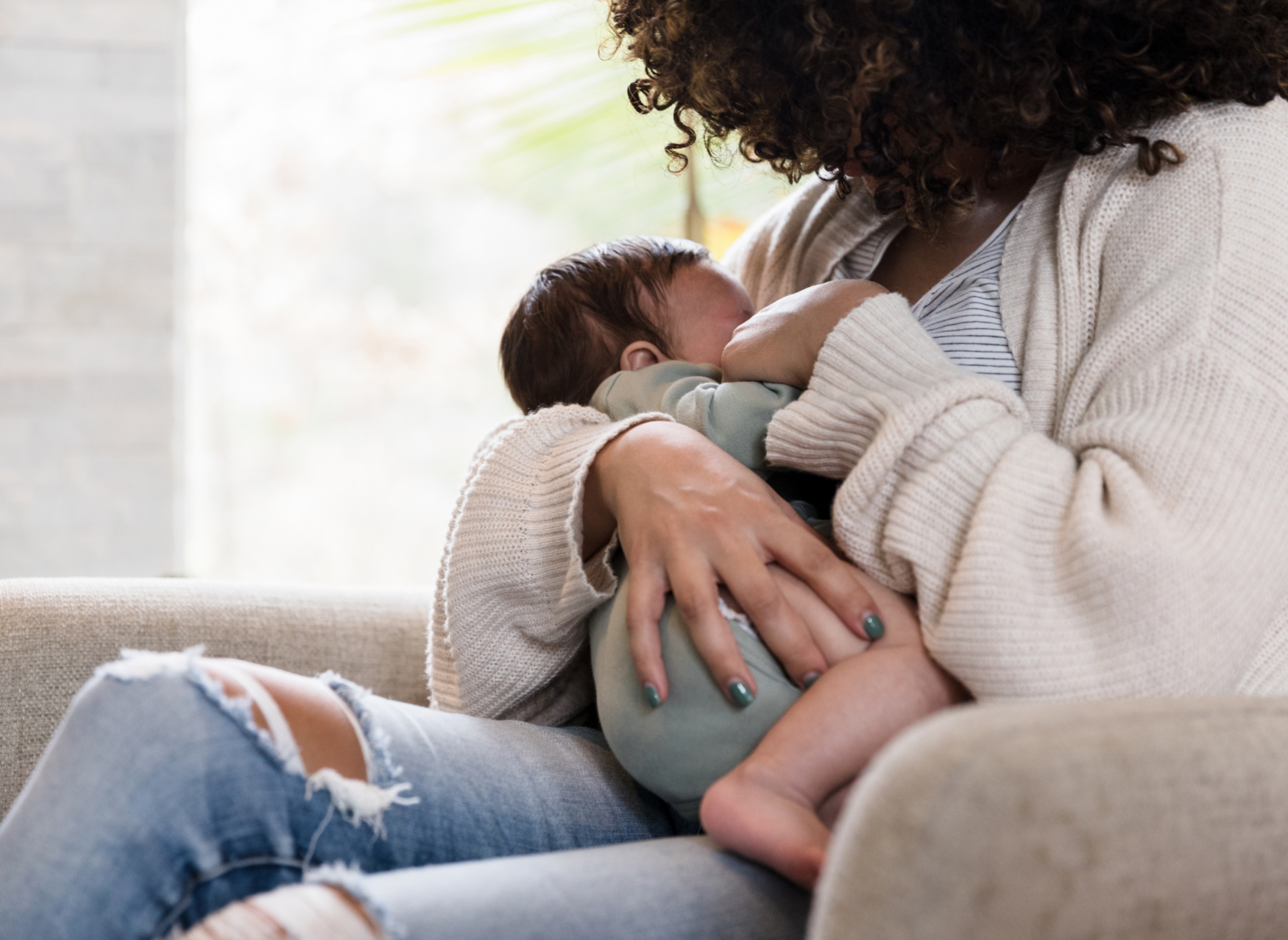 A woman sits in an armchair, holding her baby close to her chest